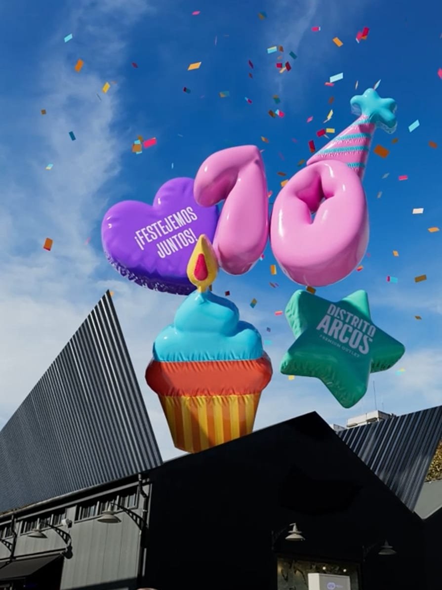 Globos inflables formando un 10 sobre Distrito Arcos, con un cupcake, un corazón y papel picado en el cielo